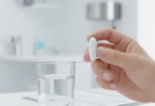 A swallowable gastric balloon capsule held in a hand next to a glass of water to illustrate the non-surgical weight loss process.